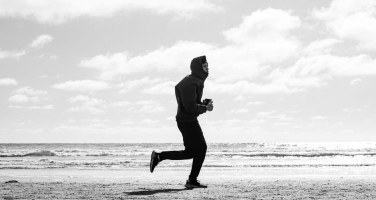 Silhouette of a jogger running along La Lucila del Mar beach, captured in monochrome.