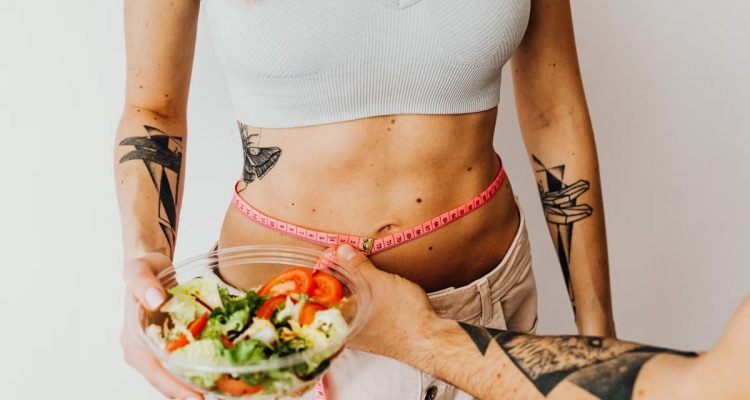 Fit woman measuring waist while holding a healthy salad bowl