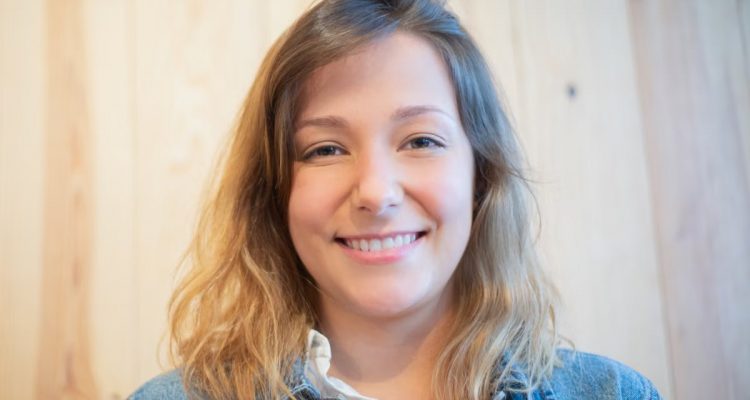 Close-up portrait of a smiling woman wearing a denim jacket with wooden background.